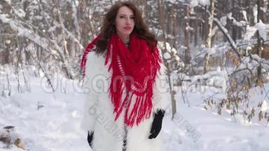迷人的金发碧眼，穿着白色的毛皮外套，戴着红领巾，在冬天的森林背景上摆着姿势。 穿白色毛皮的模特